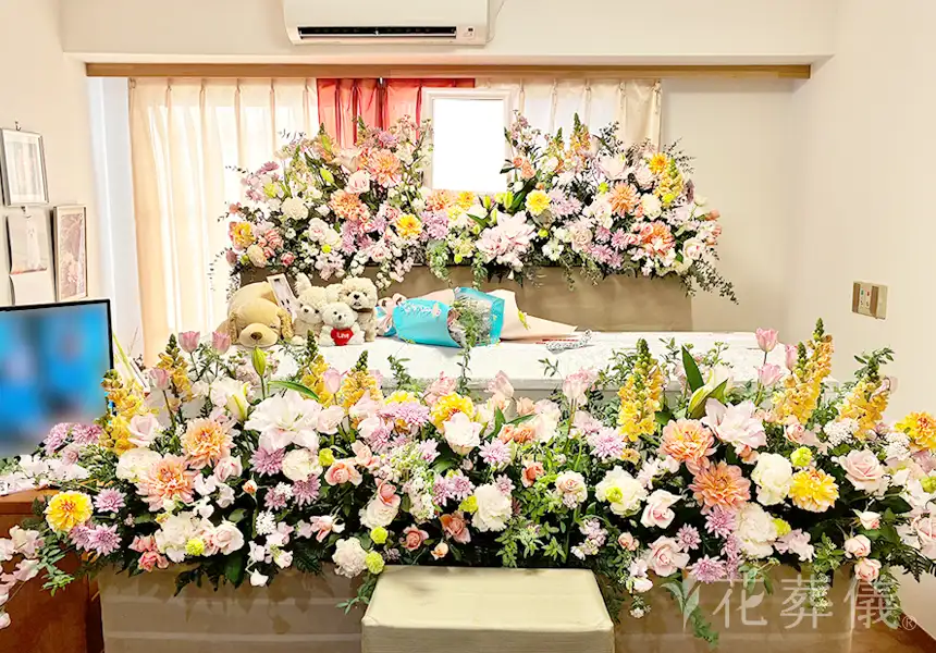 花祭壇の写真　お部屋入口から室内への廊下の両サイドにもお花を飾り、花道のようにした、あたたかみのあるオレンジやピンクのお花でワンちゃんのぬいぐるみとともにお飾りした祭壇
